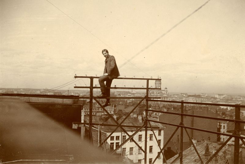 A fiatal Eric Tigerstedt egy háztetőn elhelyezett telefonkábeleket tartó emelvényen ül Helsinki felett. Háttérben látszik a Helsinki Székesegyház kupolás épülete. A kép 1905 körül készülhetett. (Forrás: Finnish Museum of Technology, Eric Tigerstedt-collection)